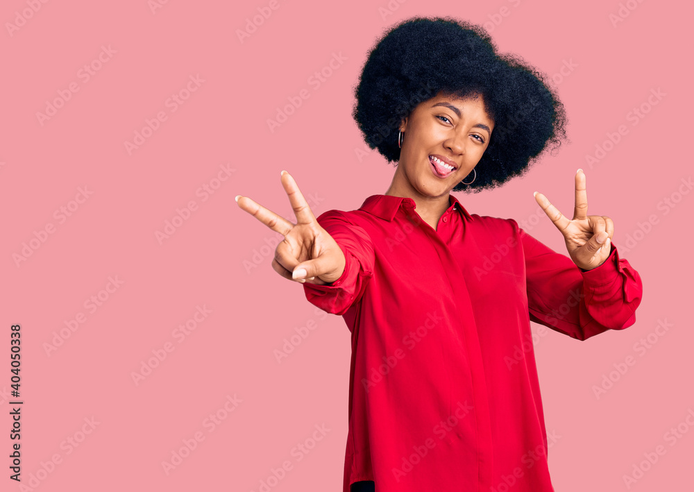 Young african american girl wearing casual clothes smiling with tongue out showing fingers of both hands doing victory sign. number two. Young african american girl wearing casual clothes smiling with tongue out showing fingers of both hands doing victory sign. number two.