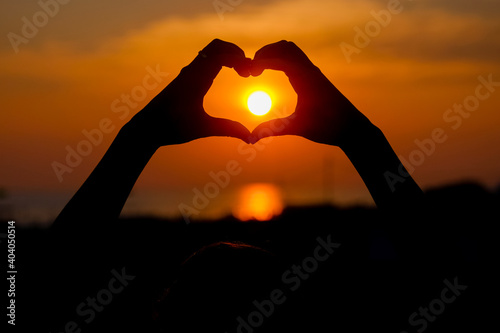 Woman hands forming a heart shape with sunset silhouette.