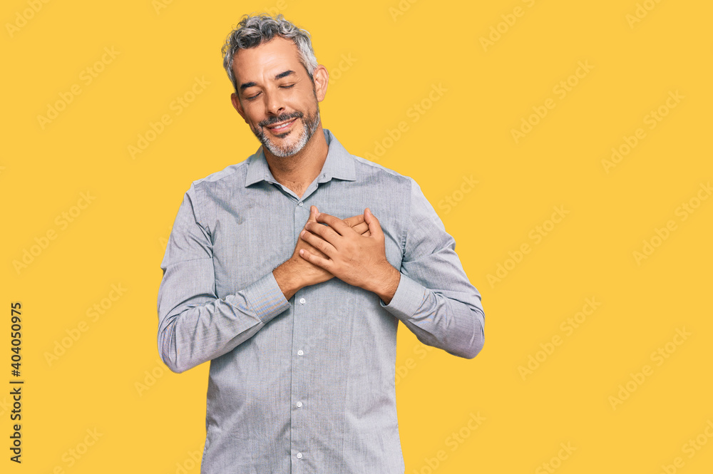 Middle age grey-haired man wearing casual clothes smiling with hands on chest with closed eyes and grateful gesture on face. health concept. Middle age grey-haired man wearing casual clothes smiling with hands on chest with closed eyes and grateful gesture on face. health concept.