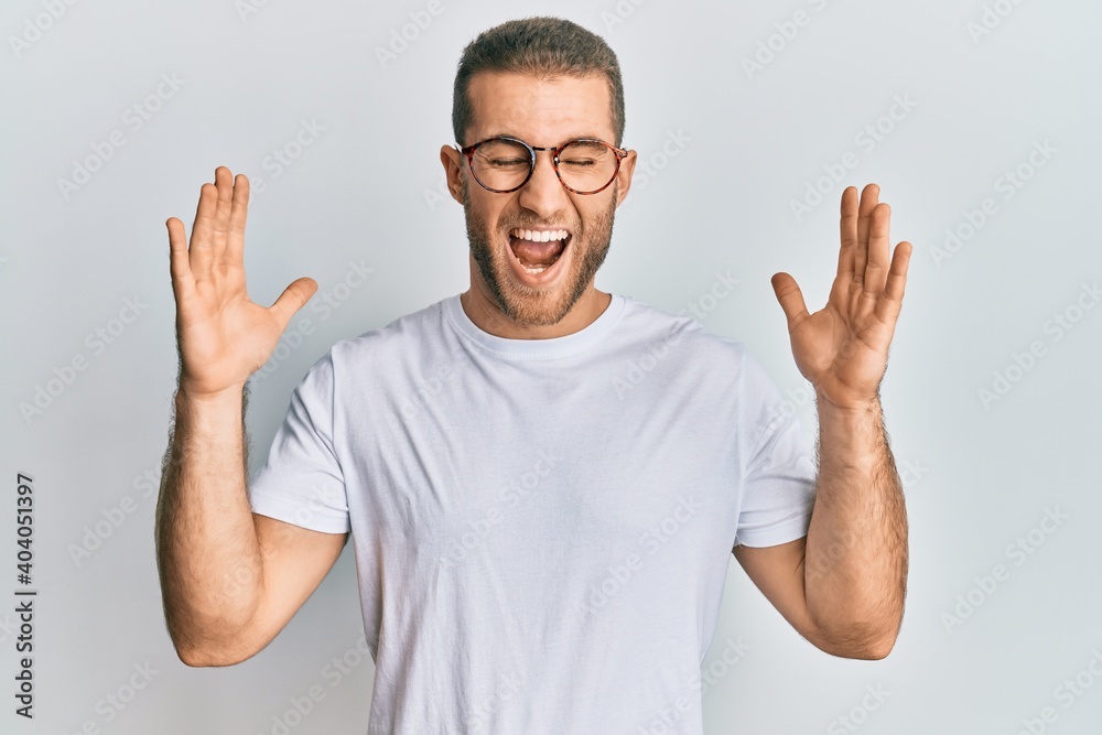 Young caucasian man wearing casual clothes and glasses celebrating mad and crazy for success with arms raised and closed eyes screaming excited. winner concept Young caucasian man wearing casual clothes and glasses celebrating mad and crazy for success with arms raised and closed eyes screaming excited. winner concept