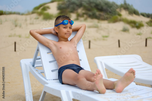 Young guy in swimming glasses is sunbathing on a sunbed on the sea beach.
