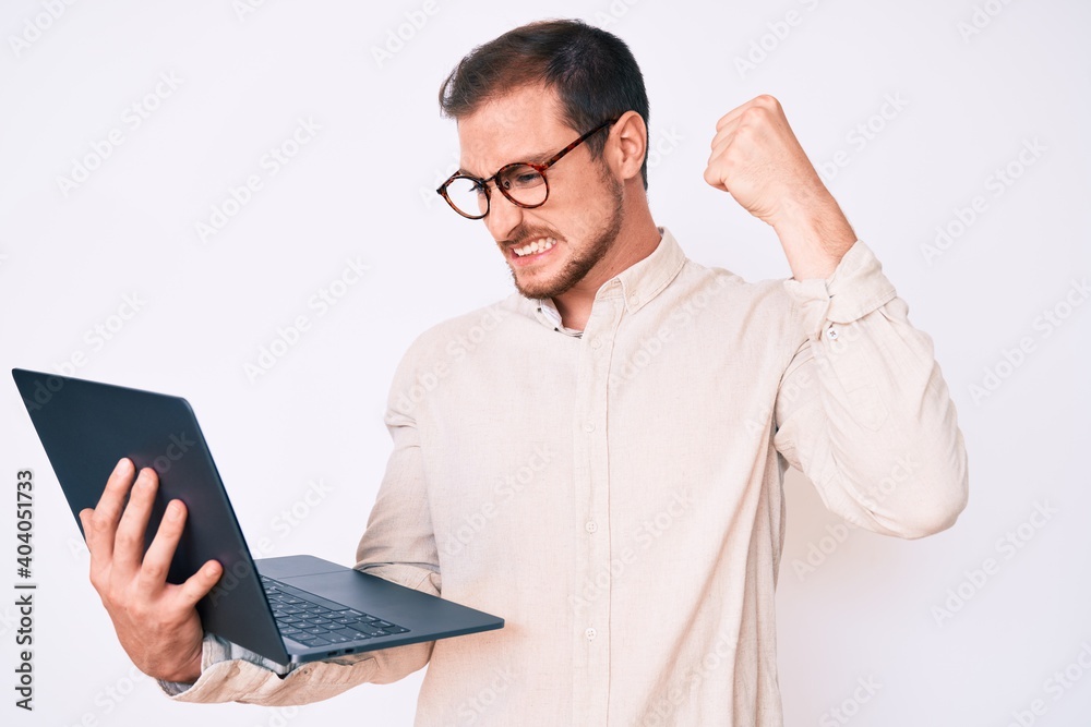 Young handsome man holding laptop annoyed and frustrated shouting with anger, yelling crazy with anger and hand raised Young handsome man holding laptop annoyed and frustrated shouting with anger, yelling crazy with anger and hand raised