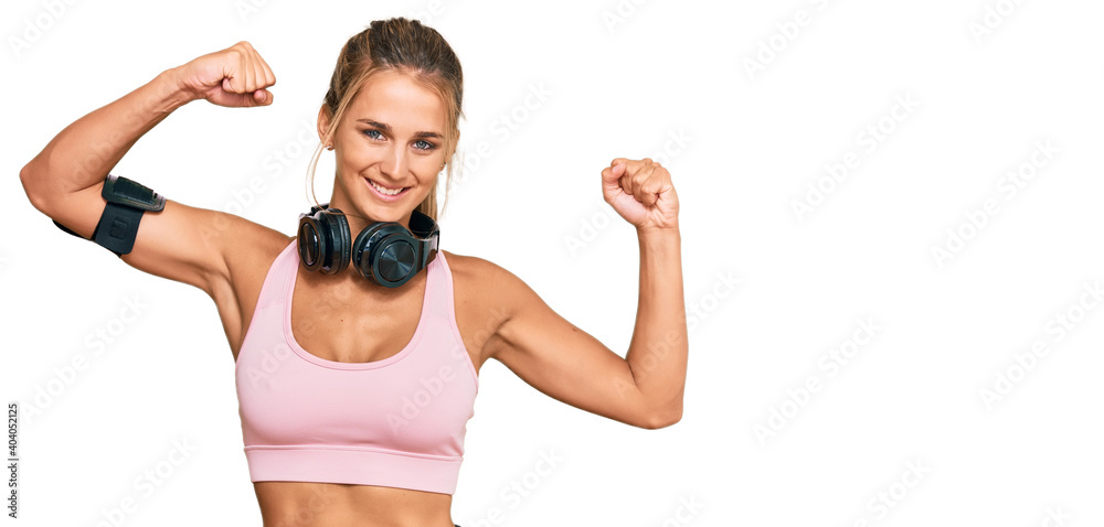 Young blonde woman wearing gym clothes and using headphones showing arms muscles smiling proud. fitness concept. Young blonde woman wearing gym clothes and using headphones showing arms muscles smiling proud. fitness concept.
