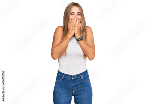 Young blonde woman wearing casual style with sleeveless shirt laughing and embarrassed giggle covering mouth with hands, gossip and scandal concept