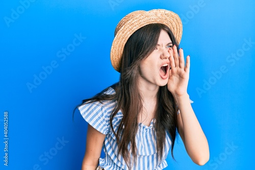 Young beautiful caucasian girl wearing summer hat shouting and screaming loud to side with hand on mouth. communication concept.