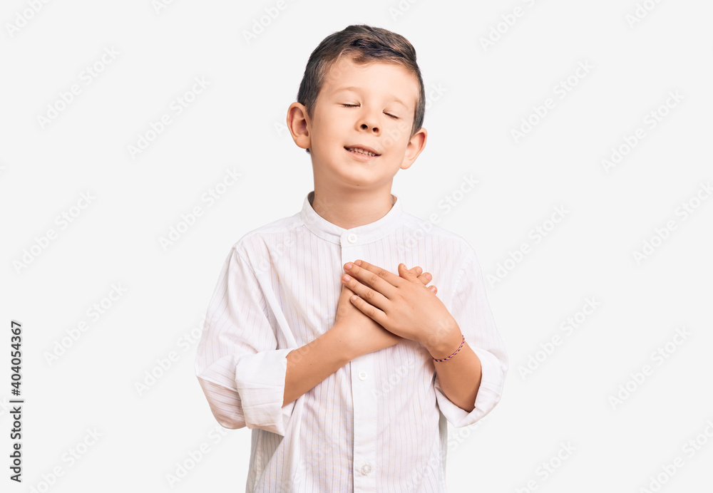 Cute blond kid wearing elegant shirt smiling with hands on chest with closed eyes and grateful gesture on face. health concept. Cute blond kid wearing elegant shirt smiling with hands on chest with closed eyes and grateful gesture on face. health concept.