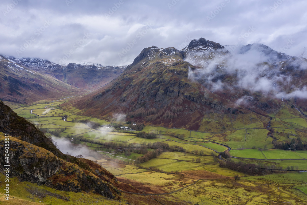 Stunning flying drone landscape image of Langdale pikes and valley in Winter with dramatic low level clouds and mist swirling around