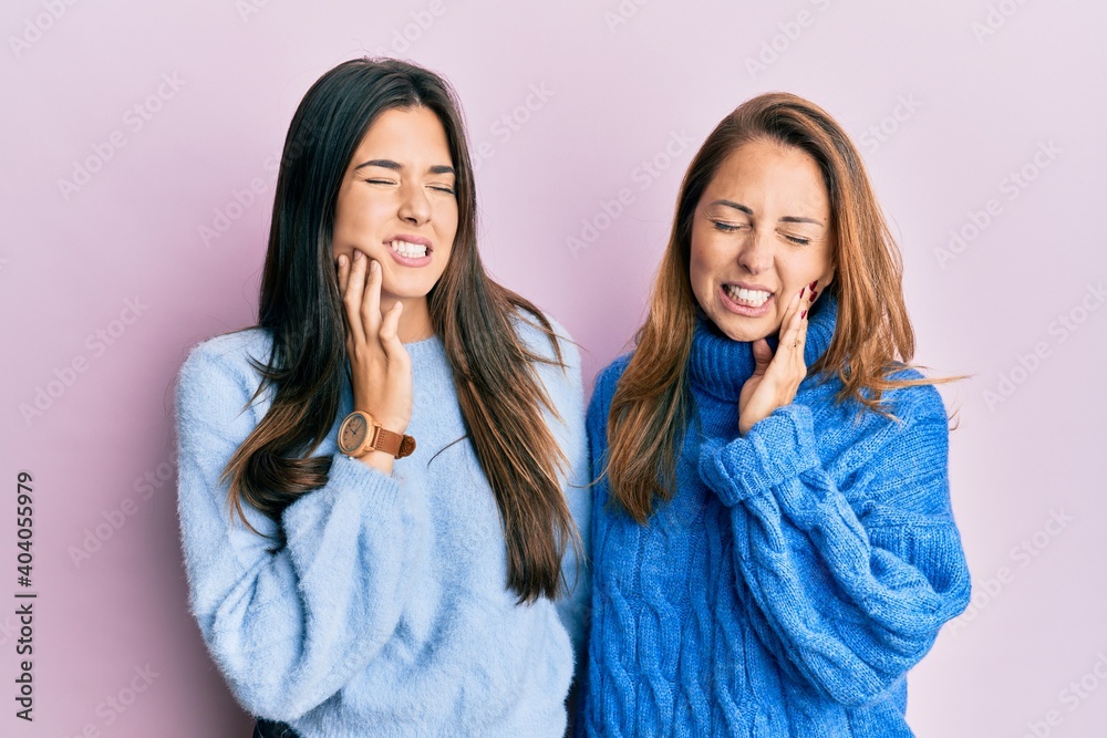 Hispanic family of mother and daughter wearing wool winter sweater touching mouth with hand with painful expression because of toothache or dental illness on teeth. dentist concept. Hispanic family of mother and daughter wearing wool winter sweater touching mouth with hand with painful expression because of toothache or dental illness on teeth. dentist concept.