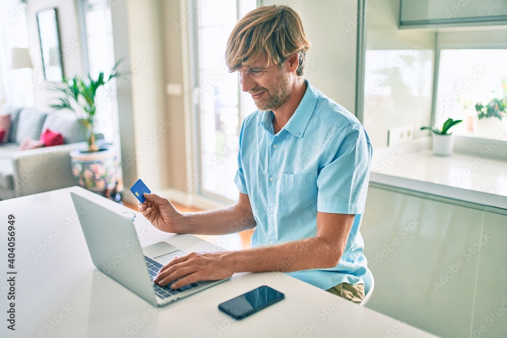 Young irish man using credit card and laptop to buy sitting on the table at home. Young irish man using credit card and laptop to buy sitting on the table at home.