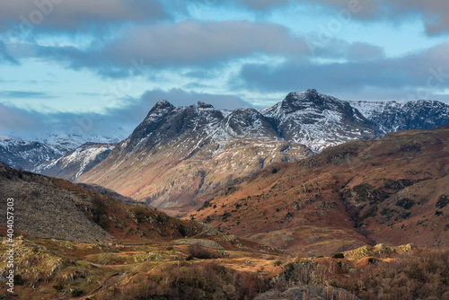 Majestic Winter landscape image view from Holme Fell in Lake District towards snow capped mountain ranges in distance in glorious evening light with Autumnal colors trees