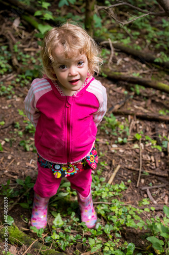 Cute blonde girl standing in a forest wearing pink jacket.