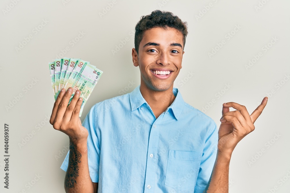 Young handsome african american man holding 50 hong kong dollars banknotes smiling happy pointing with hand and finger to the side Young handsome african american man holding 50 hong kong dollars banknotes smiling happy pointing with hand and finger to the side
