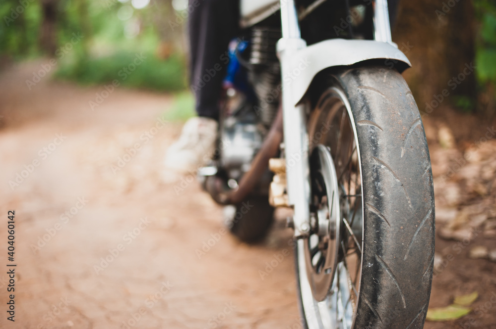 Close up the motorcycle is driving on a dirt road in the forest. Close up the motorcycle is driving on a dirt road in the forest.