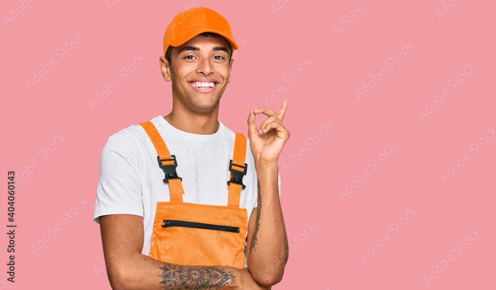 Young handsome african american man wearing handyman uniform with a big smile on face, pointing with hand and finger to the side looking at the camera. Young handsome african american man wearing handyman uniform with a big smile on face, pointing with hand and finger to the side looking at the camera.