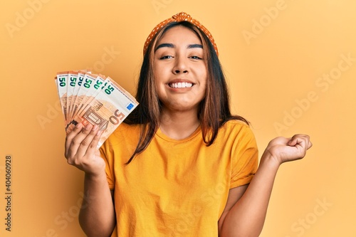 Young latin woman holding 50 euro banknotes screaming proud, celebrating victory and success very excited with raised arm