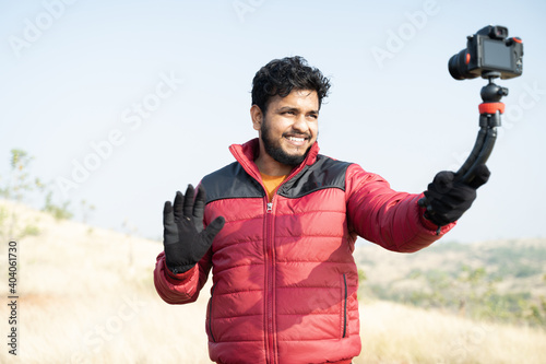 Young traveller busy talking with camera on top of Mountain - Concept of travel vlogger, blogger or influencer recording video during hiking. photo