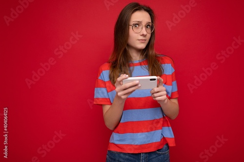 Serious attractive positive good looking young woman wearing optical glasses and casual stylish outfit poising isolated on background with empty space holding in hand and using mobile phone messaging