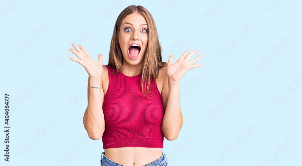 Young beautiful blonde woman wearing elegant summer shirt celebrating crazy and amazed for success with arms raised and open eyes screaming excited. winner concept