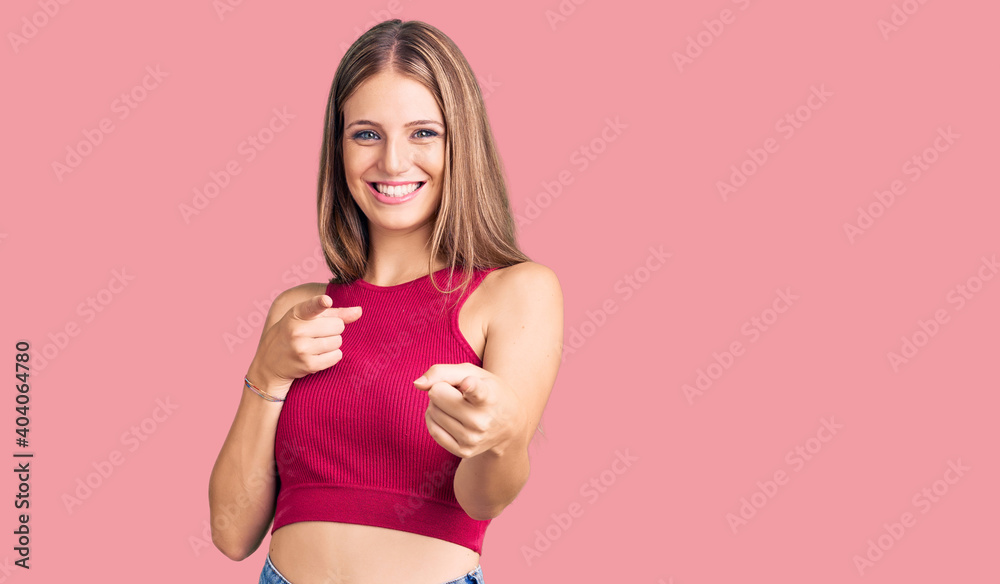 Young beautiful blonde woman wearing elegant summer shirt pointing fingers to camera with happy and funny face. good energy and vibes. Young beautiful blonde woman wearing elegant summer shirt pointing fingers to camera with happy and funny face. good energy and vibes.