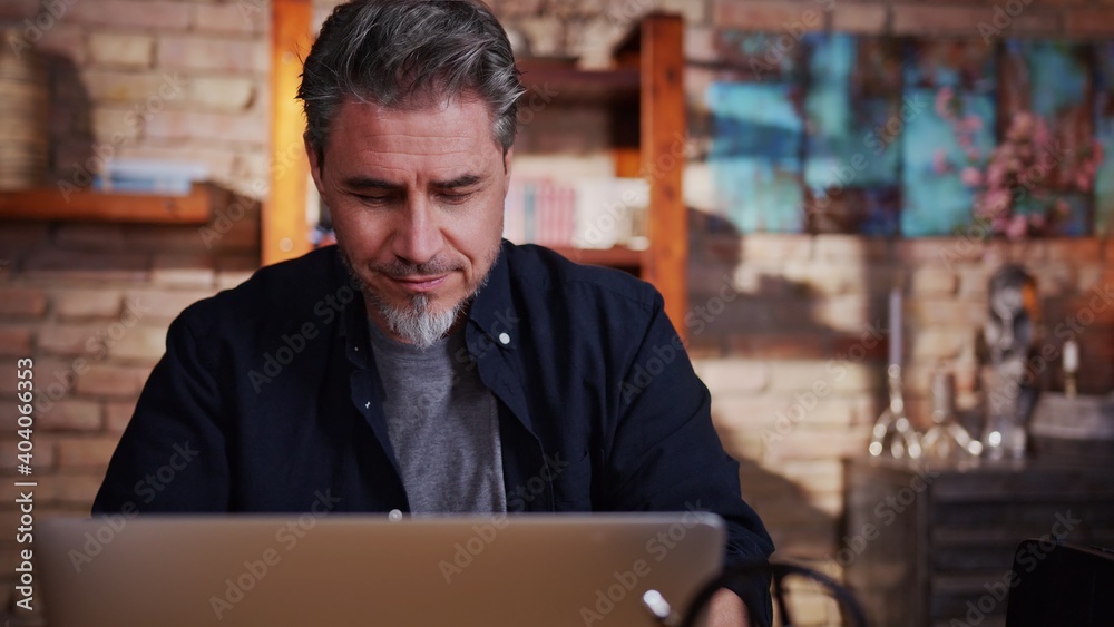 Fototapeta premium Portrait of happy mature man sitting at table using laptop at home working in home office.