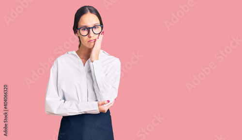 Beautiful brunette young woman wearing professional waitress apron thinking looking tired and bored with depression problems with crossed arms.