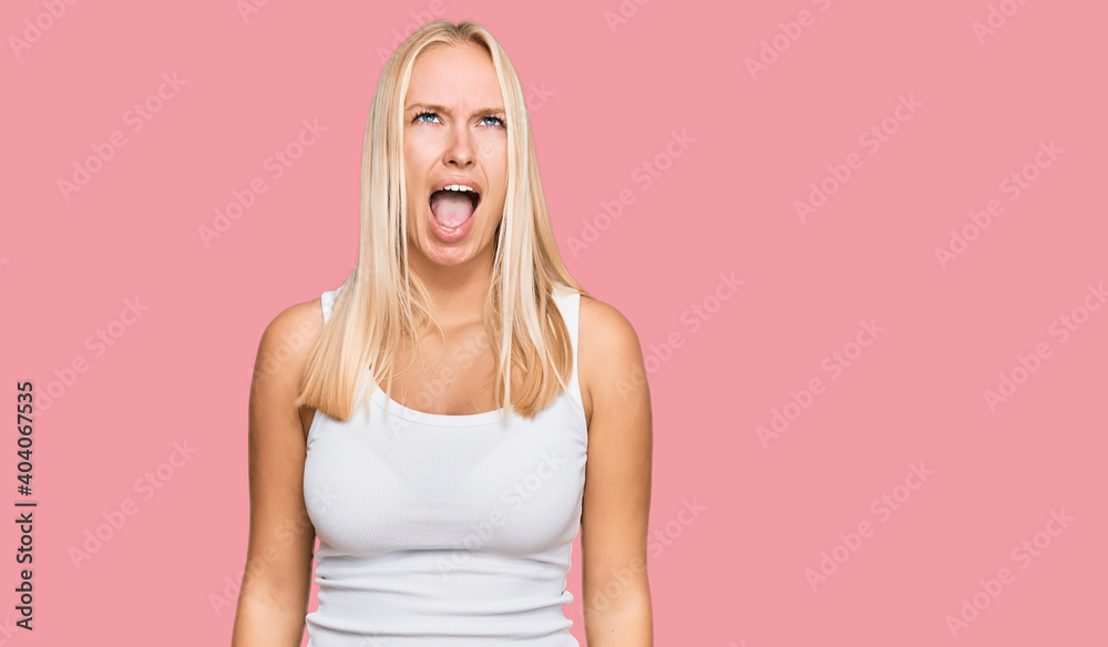 Young blonde girl wearing casual style with sleeveless shirt angry and mad screaming frustrated and furious, shouting with anger. rage and aggressive concept. Young blonde girl wearing casual style with sleeveless shirt angry and mad screaming frustrated and furious, shouting with anger. rage and aggressive concept.