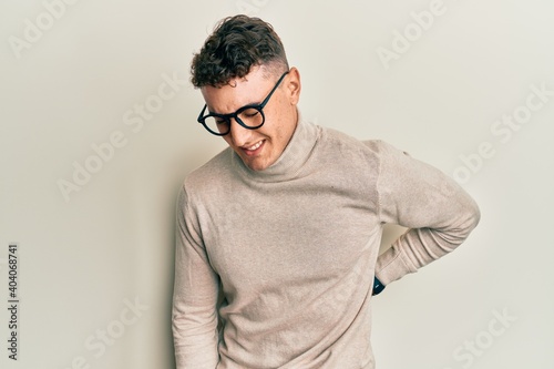 Hispanic young man wearing casual turtleneck sweater suffering of backache, touching back with hand, muscular pain