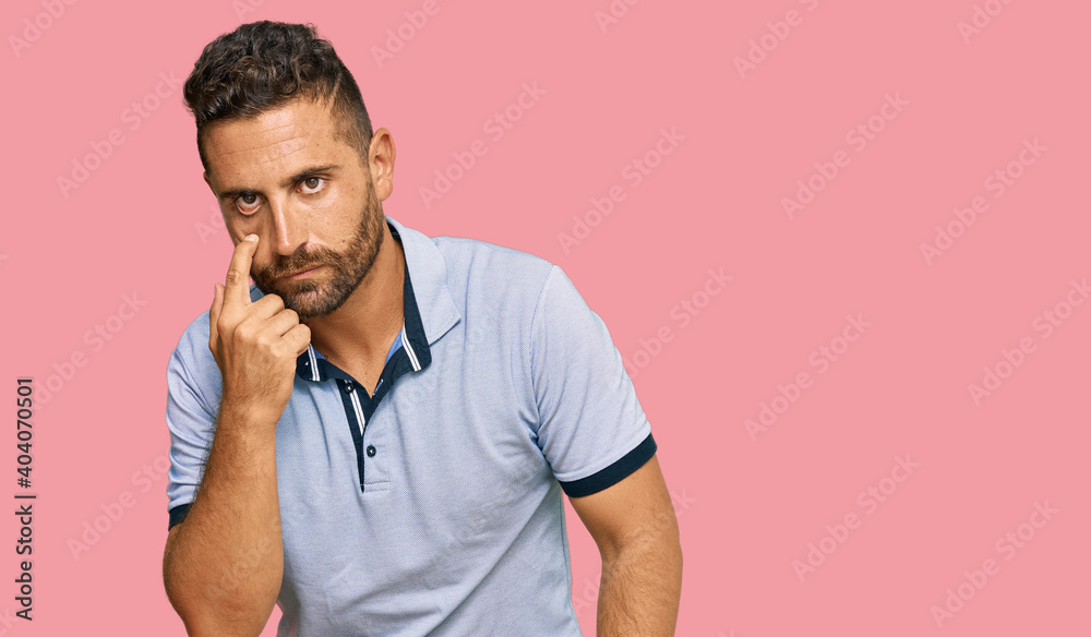 Handsome man with beard wearing casual clothes pointing to the eye watching you gesture, suspicious expression Handsome man with beard wearing casual clothes pointing to the eye watching you gesture, suspicious expression