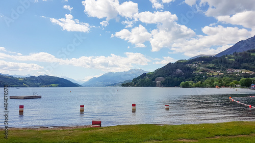 A panoramic view on the Millstaettersee lake from its shore. The lake is surrounded by high mountains. The Alpine lake is waving gently. A few buoys drifting on its surface. Serenity and calmness