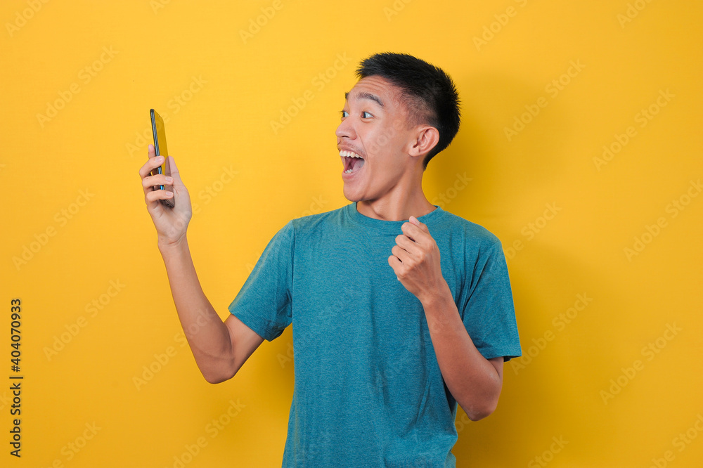 Shocked face of Asian man in casual blue t-shirt looking at phone screen Shocked face of Asian man in casual blue t-shirt looking at phone screen