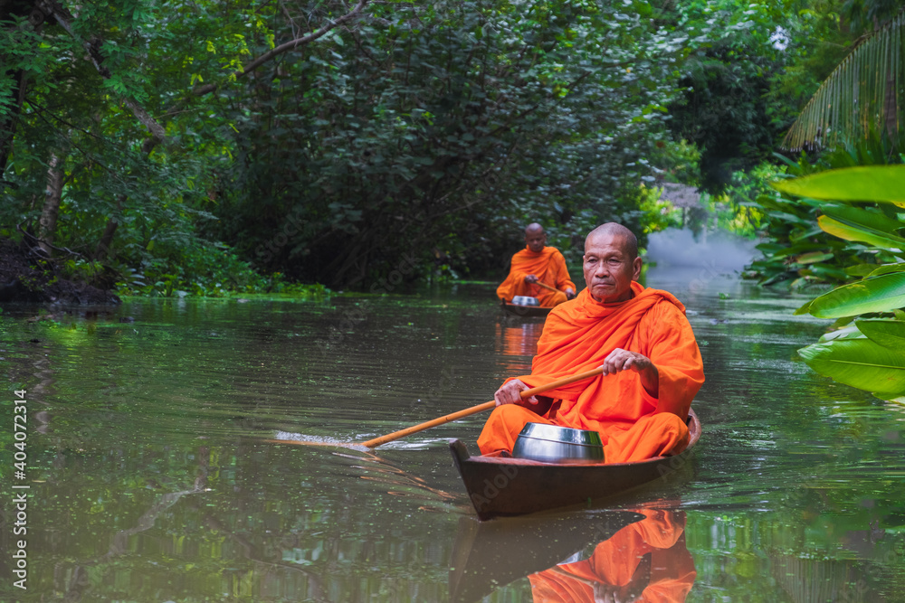 Monks rowing alms on the canal in the morning Through a tree tunnel In the water there is a reflection,The culture tradition Buddhist monk of making merit .