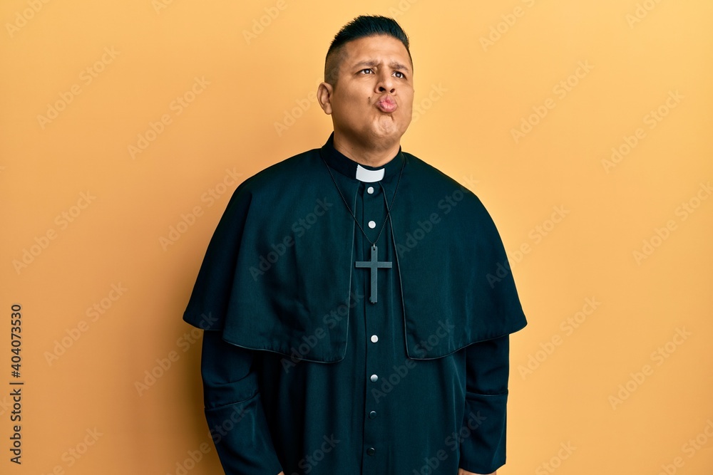 Obraz premium Young latin priest man standing over yellow background looking at the camera blowing a kiss on air being lovely and sexy. love expression.