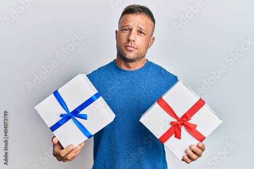 Handsome muscle man holding gifts clueless and confused expression. doubt concept.