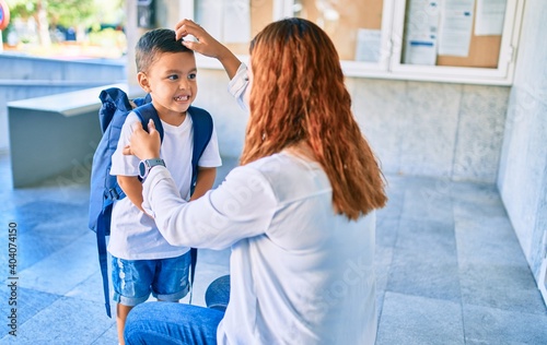 Adorable latin student boy and mom at school. Mother preparing kid putting up backpack.
