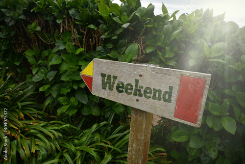 vintage old wooden signboard with text weekend near the green plants.