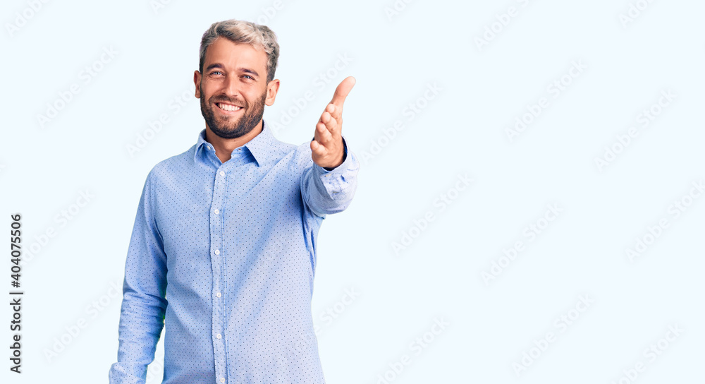 Young handsome blond man wearing elegant shirt smiling friendly offering handshake as greeting and welcoming. successful business. Young handsome blond man wearing elegant shirt smiling friendly offering handshake as greeting and welcoming. successful business.
