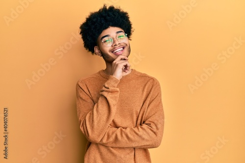 Young african american man with afro hair wearing casual winter sweater looking confident at the camera with smile with crossed arms and hand raised on chin. thinking positive. © Krakenimages.com