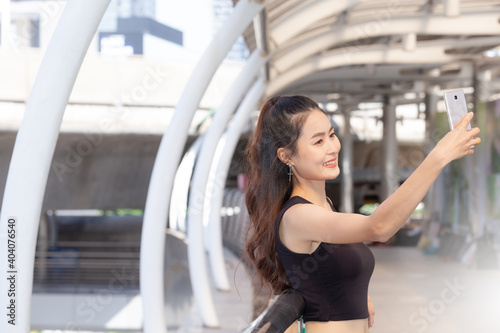 Portrait happy young sporty woman taking  selfie at skywalk. She looking at smart phone, wearing  black sportwear GYM. Relaxing and Smiling concept. © nchamunee