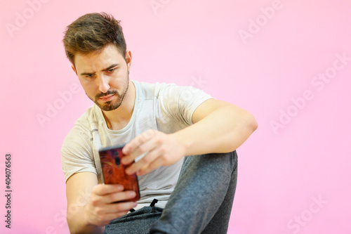 Guy seated on the floor using smartphone, on pink pastel color background. High quality photo
