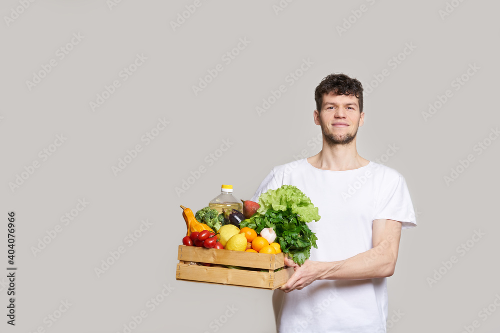 online shopping concept. A man in T-shirt holds a box of fresh food in his hands. Food delivery from the supermarket, from farmers. Delivery during quarantine online shopping concept. A man in T-shirt holds a box of fresh food in his hands. Food delivery from the supermarket, from farmers. Delivery during quarantine