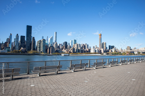 Midtown Manhattan Skyline with a Long Row of Empty Park Benches along the Riverfront of Long Island City Queens New York