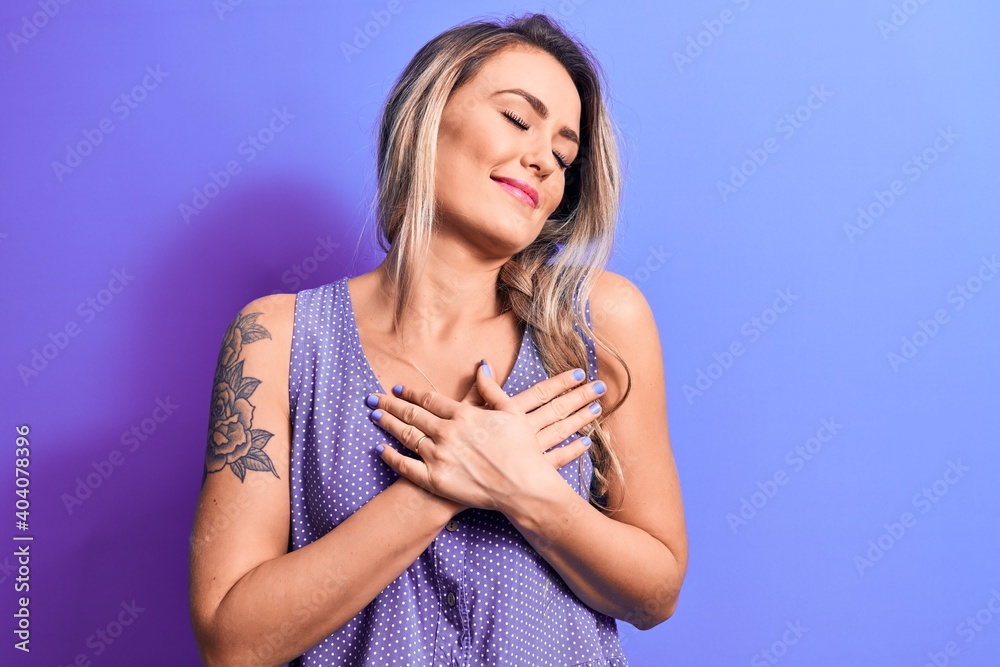 Young beautiful blonde woman wearing casual t-shirt standing over isolated purple background smiling with hands on chest, eyes closed with grateful gesture on face. Health concept. Young beautiful blonde woman wearing casual t-shirt standing over isolated purple background smiling with hands on chest, eyes closed with grateful gesture on face. Health concept.
