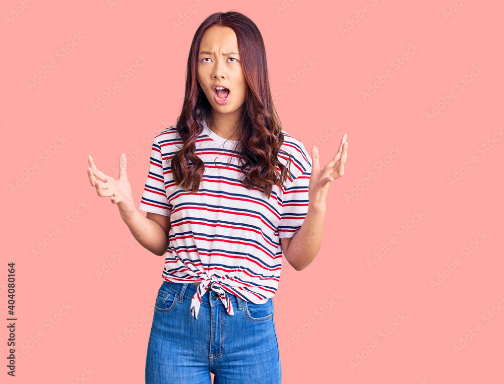 Young beautiful chinese girl wearing casual clothes crazy and mad shouting and yelling with aggressive expression and arms raised. frustration concept. Young beautiful chinese girl wearing casual clothes crazy and mad shouting and yelling with aggressive expression and arms raised. frustration concept.