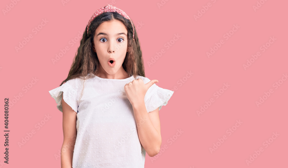 Cute hispanic child girl wearing casual white tshirt surprised pointing with hand finger to the side, open mouth amazed expression. Cute hispanic child girl wearing casual white tshirt surprised pointing with hand finger to the side, open mouth amazed expression.