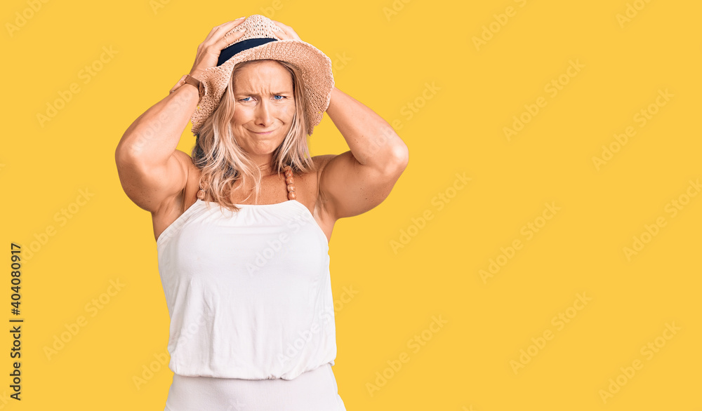 Middle age fit blonde woman wearing summer hat suffering from headache desperate and stressed because pain and migraine. hands on head. Middle age fit blonde woman wearing summer hat suffering from headache desperate and stressed because pain and migraine. hands on head.