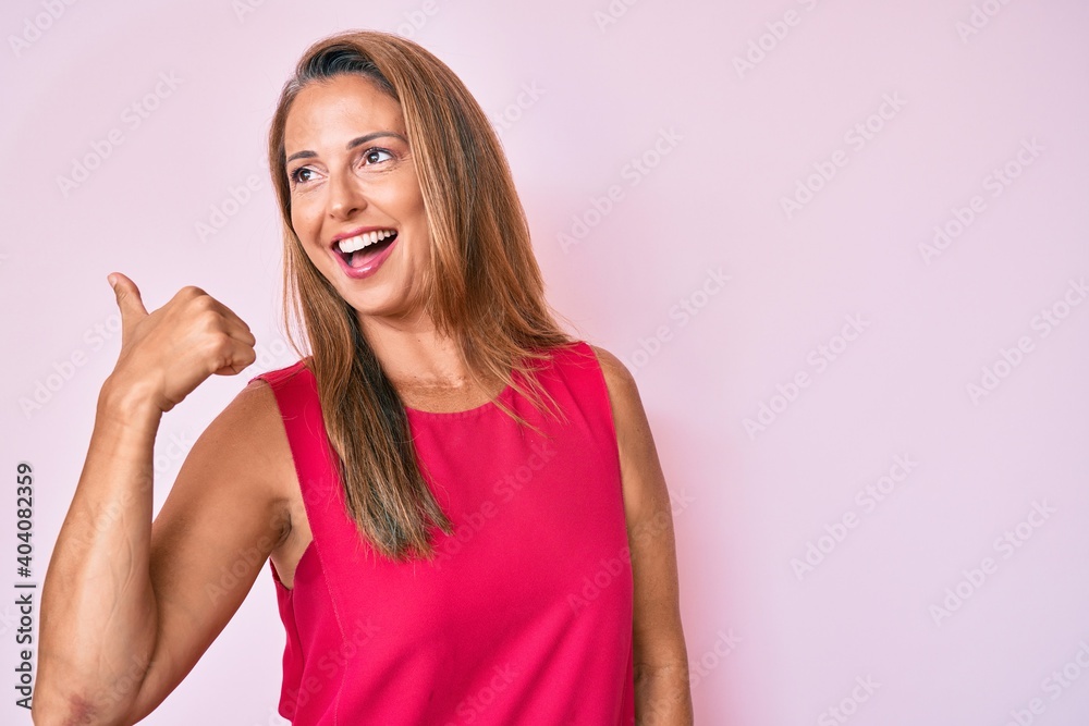 Middle age hispanic woman wearing casual clothes pointing thumb up to the side smiling happy with open mouth Middle age hispanic woman wearing casual clothes pointing thumb up to the side smiling happy with open mouth
