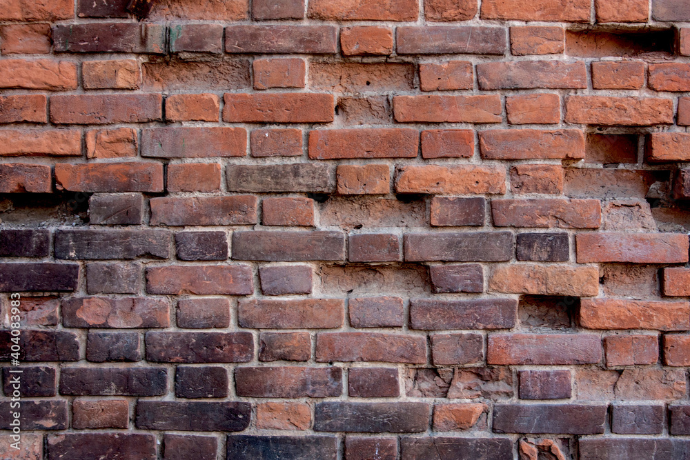 Obraz premium The wall is made of red brick with traces of burning and destroyed bricks