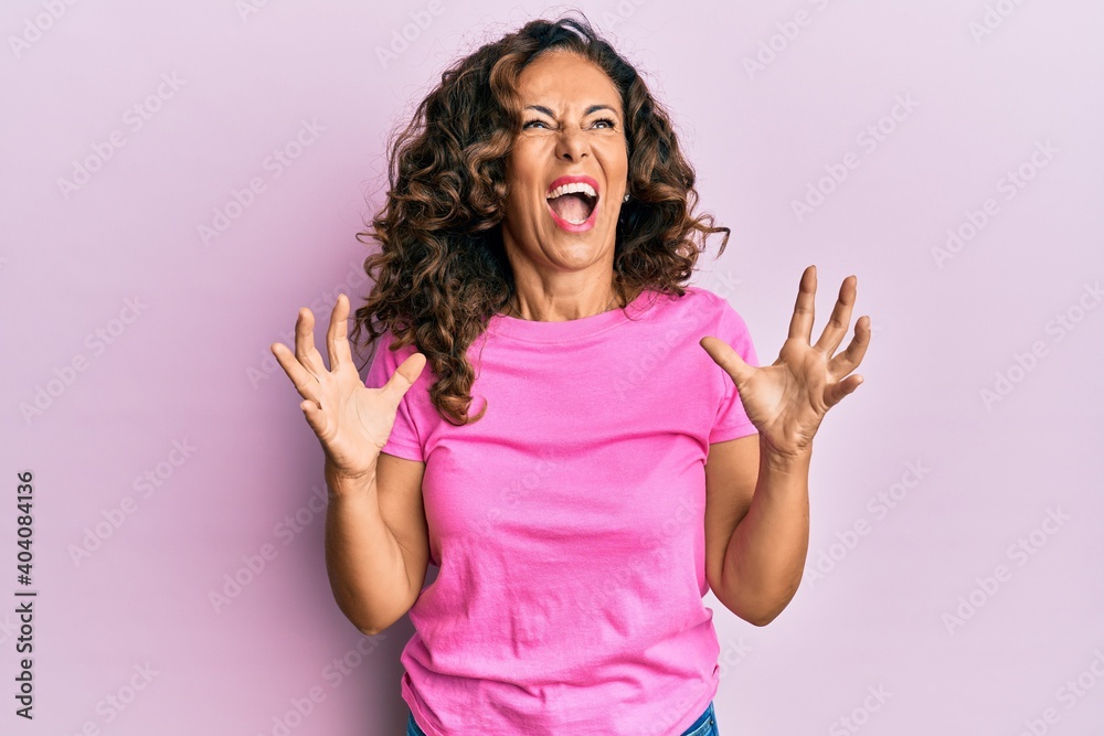 Middle age hispanic woman wearing casual clothes crazy and mad shouting and yelling with aggressive expression and arms raised. frustration concept. Middle age hispanic woman wearing casual clothes crazy and mad shouting and yelling with aggressive expression and arms raised. frustration concept.