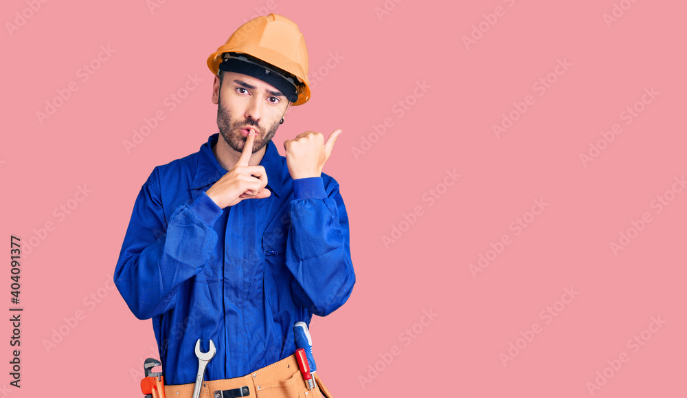 Young hispanic man wearing worker uniform asking to be quiet with finger on lips pointing with hand to the side. silence and secret concept. Young hispanic man wearing worker uniform asking to be quiet with finger on lips pointing with hand to the side. silence and secret concept.