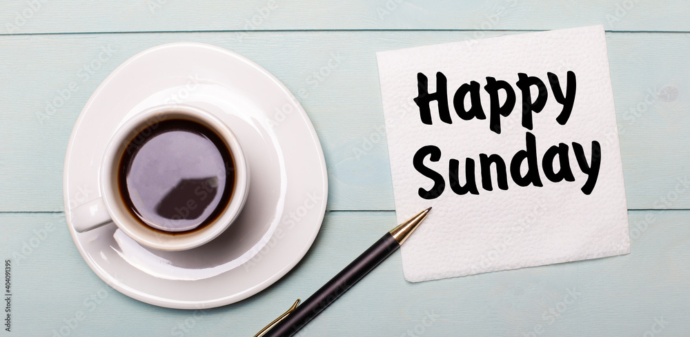 On a light blue wooden tray, there is a white cup of coffee, a handle and a napkin that says HAPPY SUNDAY. On a light blue wooden tray, there is a white cup of coffee, a handle and a napkin that says HAPPY SUNDAY.